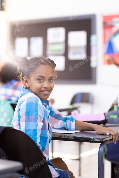 Preview: Vertical portrait of smiling biracial schoolgirl sitting at desk turning round in class copy space