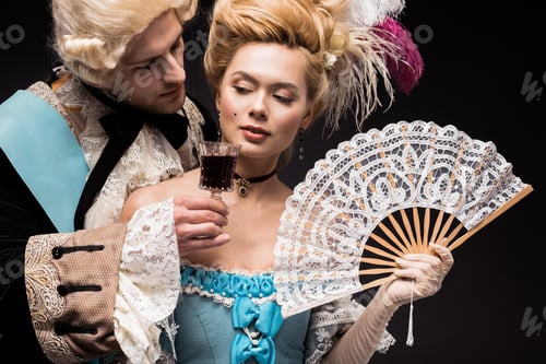 Preview: handsome man looking at young victorian woman in wig holding fan and wine glass isolated on black