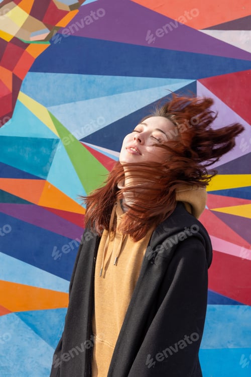 Preview: A young creative woman stands against the backdrop of a bright, colorful, multi-colored wall.