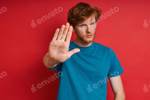 Preview: Confident redhead man gesturing stop sign while standing against red background