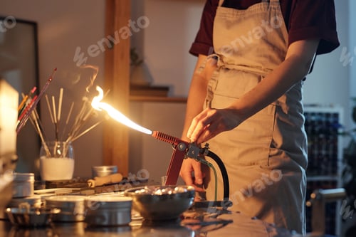 Preview: Hands of female lampworker in apron standing by workplace and regulating burner