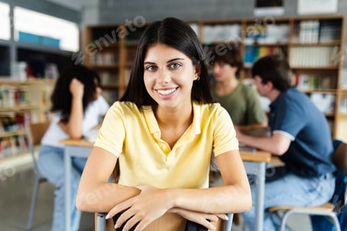 Preview: Young happy female student smiling at camera sitting on chair at library