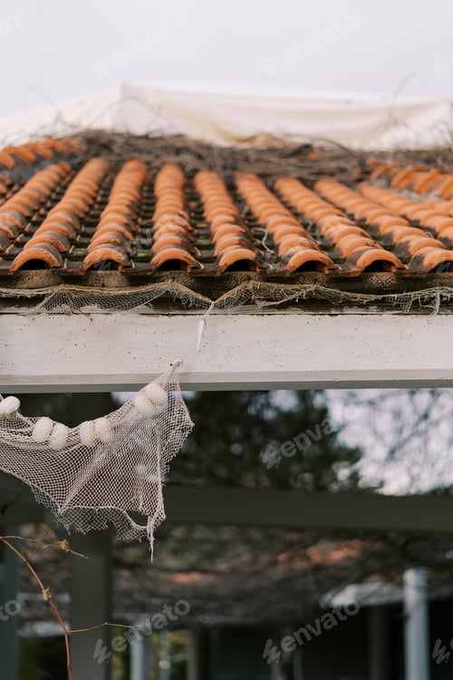 Preview: Old fishing net hangs from a wooden beam under a red tiled roof