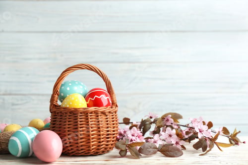 Preview: Painted Easter eggs in wicker basket and blossoming branches on table. Space for text