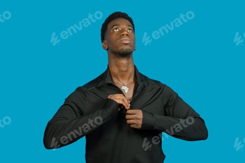 Preview: Young black man zipping his sports jacket looking upwards on blue background