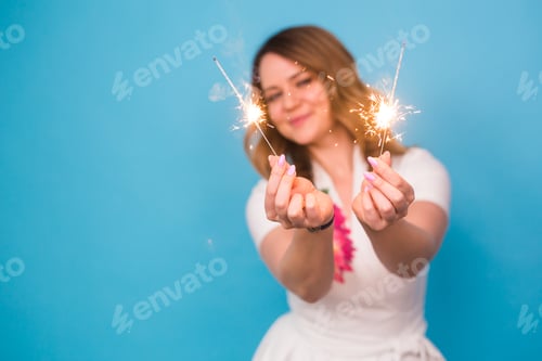Preview: Portrait of a happy woman holding bengal lights over blue background with copy space. Christmas