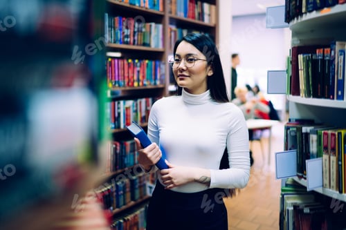 Preview: Ethnic young student standing with blue book in college library