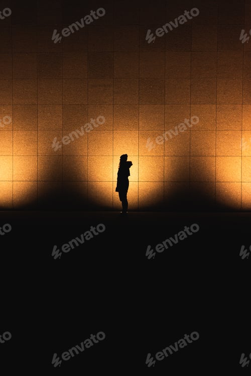 Preview: Silhouette of a woman standing in front of 3 illuminated lights at night