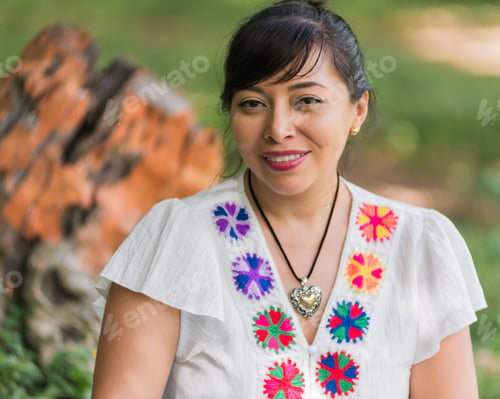 Preview: A portrait of a smiling woman wearing a white blouse adorned with colorful embroidered flowers