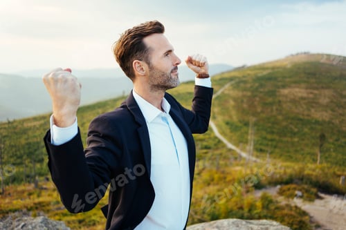 Preview: Self-confident businessman standing on top of a mountain