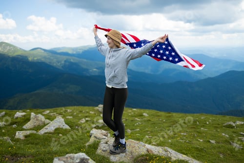 Preview: Woman holding USA flag on top of mountain and enjoys the view of the autumn rocks hills