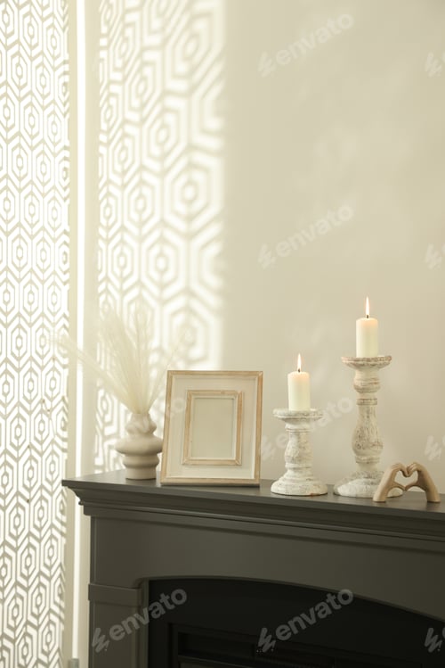 Preview: Stylish candlesticks with burning candles and other decor on fireplace near white wall indoors