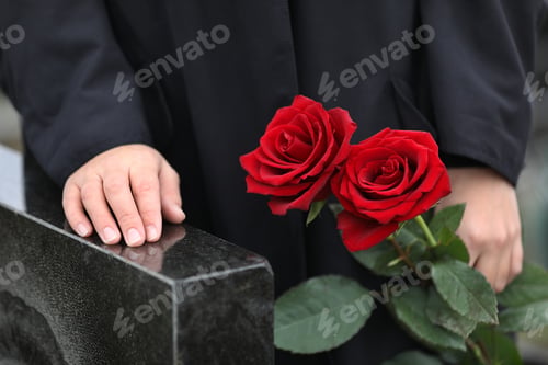 Preview: Woman with red roses near black granite tombstone outdoors, closeup. Funeral ceremony
