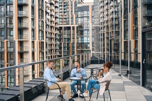 Preview: Group of businesspeople sitting around coffee table outside