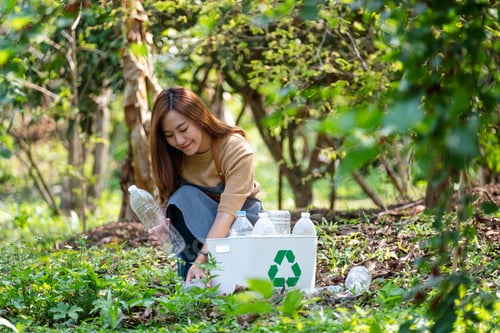 Preview: asian woman collecting and putting plastic bottles into a recycle bin in the outdoors
