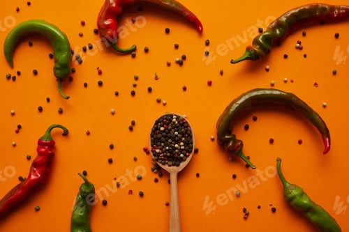 Preview: top view of chili peppers and peppercorns in wooden spoon on orange