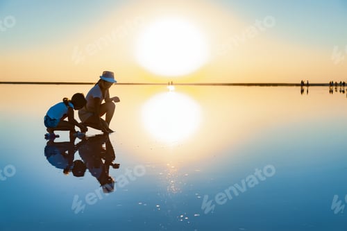 Preview: Two girls on a beautiful transparent lake are looking for something in a shiny surface