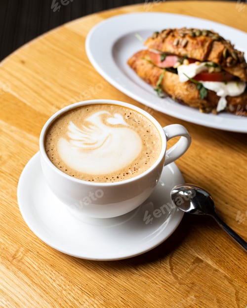 Preview: a cup of cappuccino in a cafe stands on a wooden table. in the background croissant with tomatoes