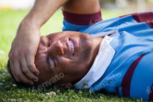 Preview: Injured rugby player with eyes closed lying on field