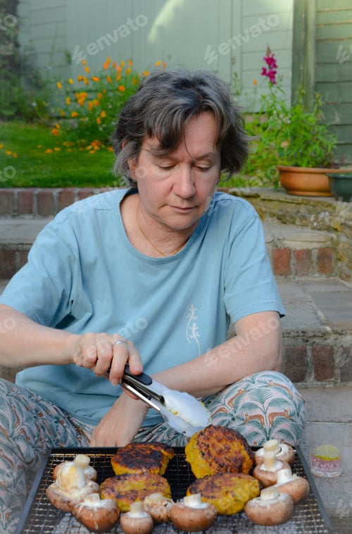 Preview: Woman in garden, cooking chicken cats burgers and mushrooms on barbecue
