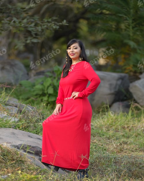 Preview: A woman stands outdoors, posed against a backdrop of greenery and rocks