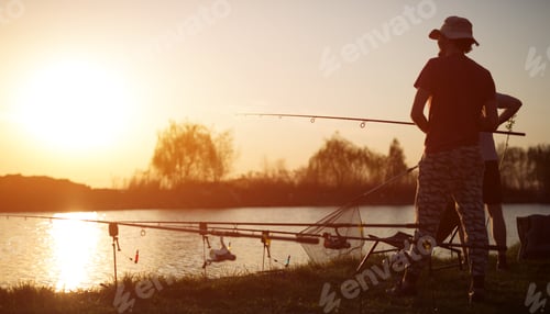 Preview: Young man fishing on lake at sunset enjoying hobby