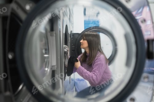 Preview: Woman using washing machine in a self-service public laundry