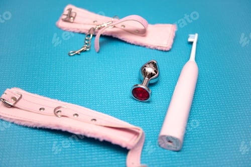 Preview: Sex toys on a blue background. Anal plug with pink handcuffs and electric toothbrush. Household appl