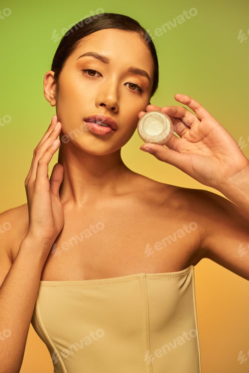 Preview: beauty product, young asian woman with bare shoulders holding cosmetic jar with face cream on green
