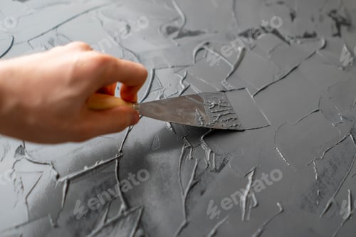 Preview: close up hand with spatula or putty knife put gray putty on the wall, decorating processs