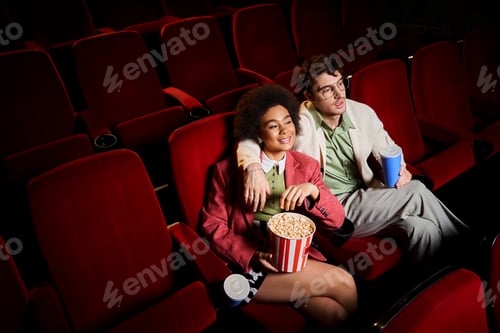 Preview: good looking joyful diverse couple in retro stylish attires watching movie on date at cinema