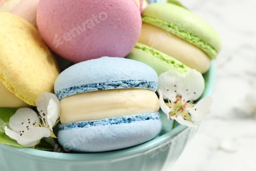Preview: Delicious colorful macarons and flowers in bowl on table, closeup