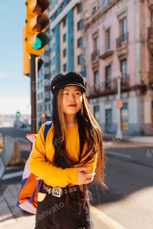 Preview: young asian girl waits by a traffic light to cross the road in a city.