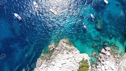 Preview: Aerial view of boats on clear blue water near a rocky coast.