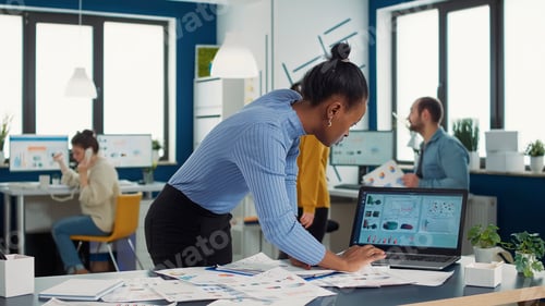 Preview: Busy african american in startup putting clipboard on desk looking at papers with sales charts