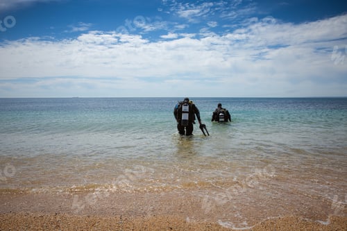 Preview: Two deep sea divers wearing oxygen tanks and wetsuits walking into the ocean from a beach