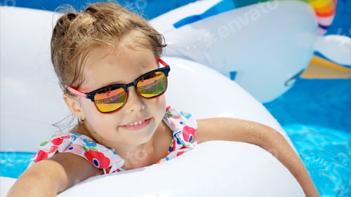 Preview: Little girl in sunglasses resting on white pool balloon