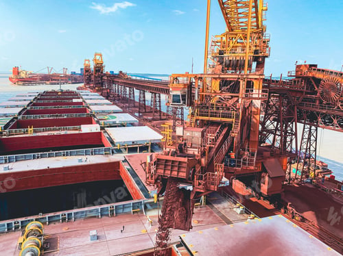 Preview: Iron ore conveyor loading cargo in the bulk carrier with a cloudy blue sky in the background