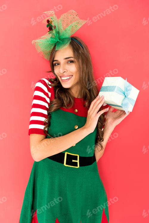 Preview: portrait of smiling woman in elf costume with christmas gift isolated on red