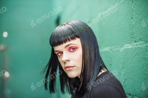 Preview: Portrait of woman leaning against painted breeze block wall looking at camera