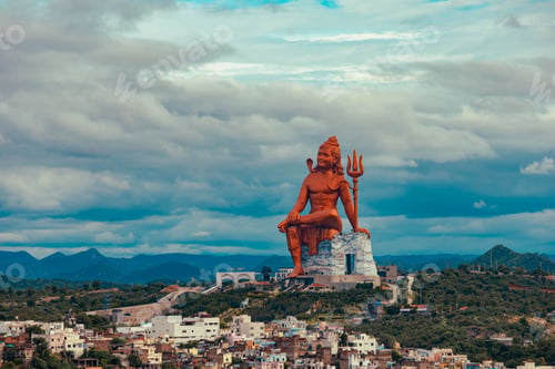 Preview: Big, red Shiva sculpture sitting on one rock and the cityscape of Nathdwara