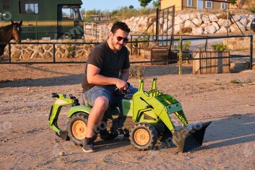 Preview: Man in sunglasses on toy tractor.