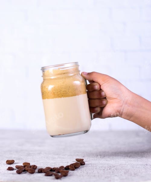 Preview: Person holding a jar of caramel smoothie over coffee beans behind a white background