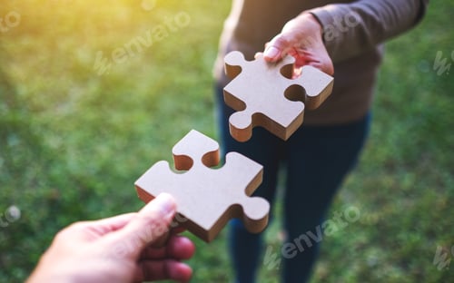 Preview: Closeup image of two people holding and putting a piece of wooden jigsaw puzzle together