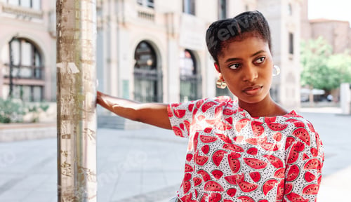 Preview: Young woman looking away while holding on to a pillar on the street.
