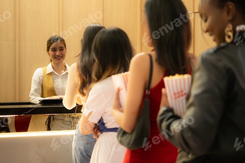 Preview: Young asian woman standing in line to buy movie tickets and in hand popcorn and drink,