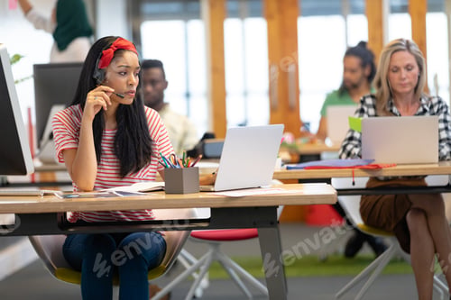 Preview: Beautiful Mixed-race female customer service executive talking on headset and working on laptop