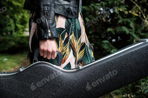 Preview: Close up of woman arm holding a guitar case in a park.