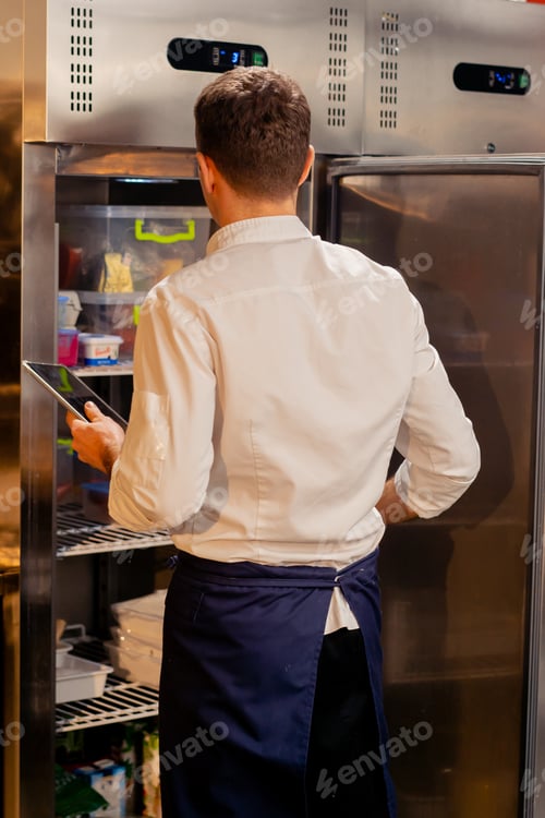 Preview: professional kitchen chef looks into the fridge and chooses ingredients for cooking food concept