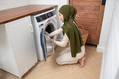 Preview: Muslim woman wearing hijab doing laundry in home